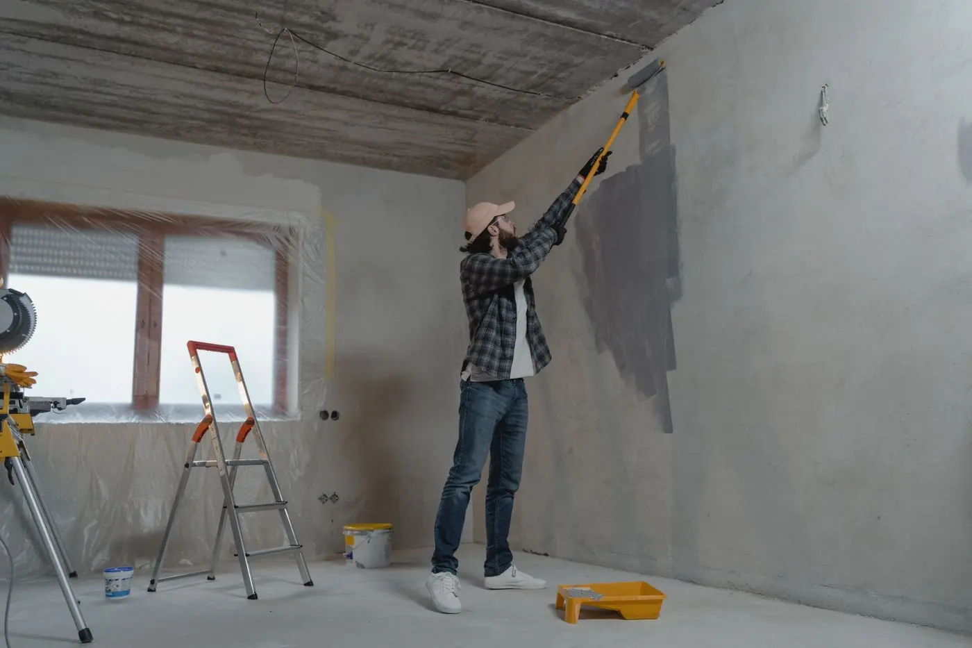 Man verft een grijze muur met een verfroller op lange steel